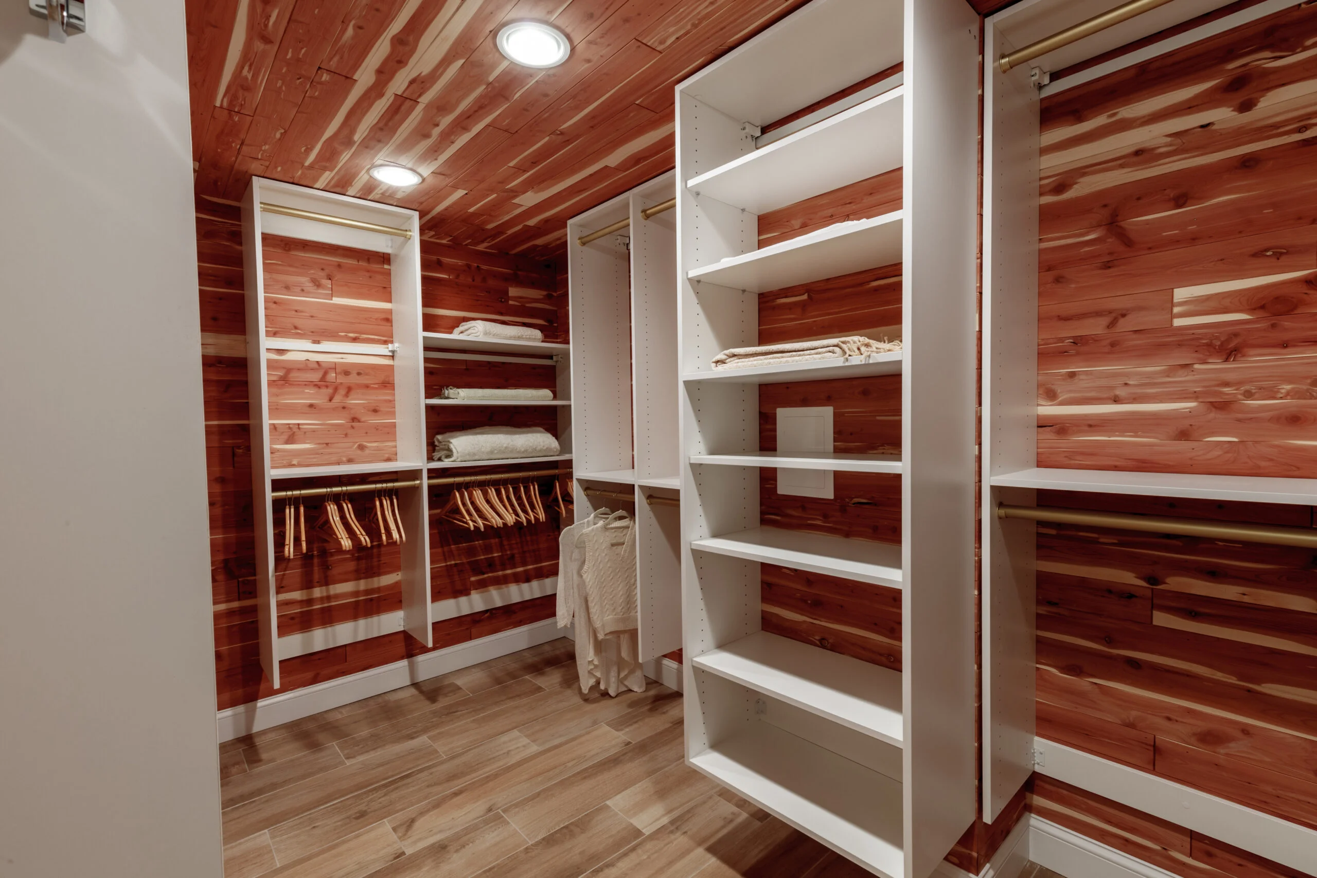 Walk-in closet with cedar walls and ceiling, white shelving, gold hanging rods, and wood-look tile flooring.