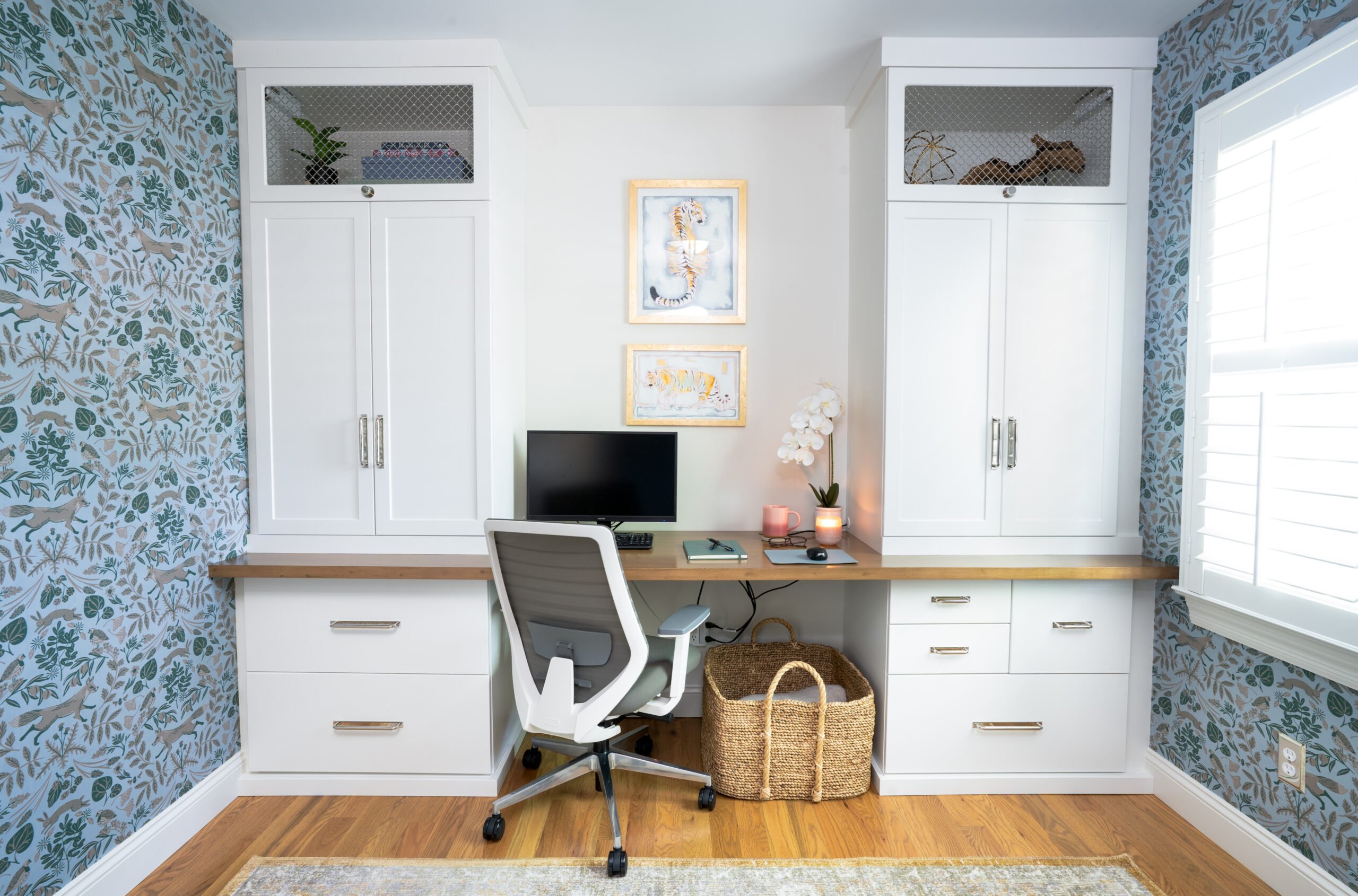 Built-in white desk with wooden countertop, gray chair, and patterned wallpaper.