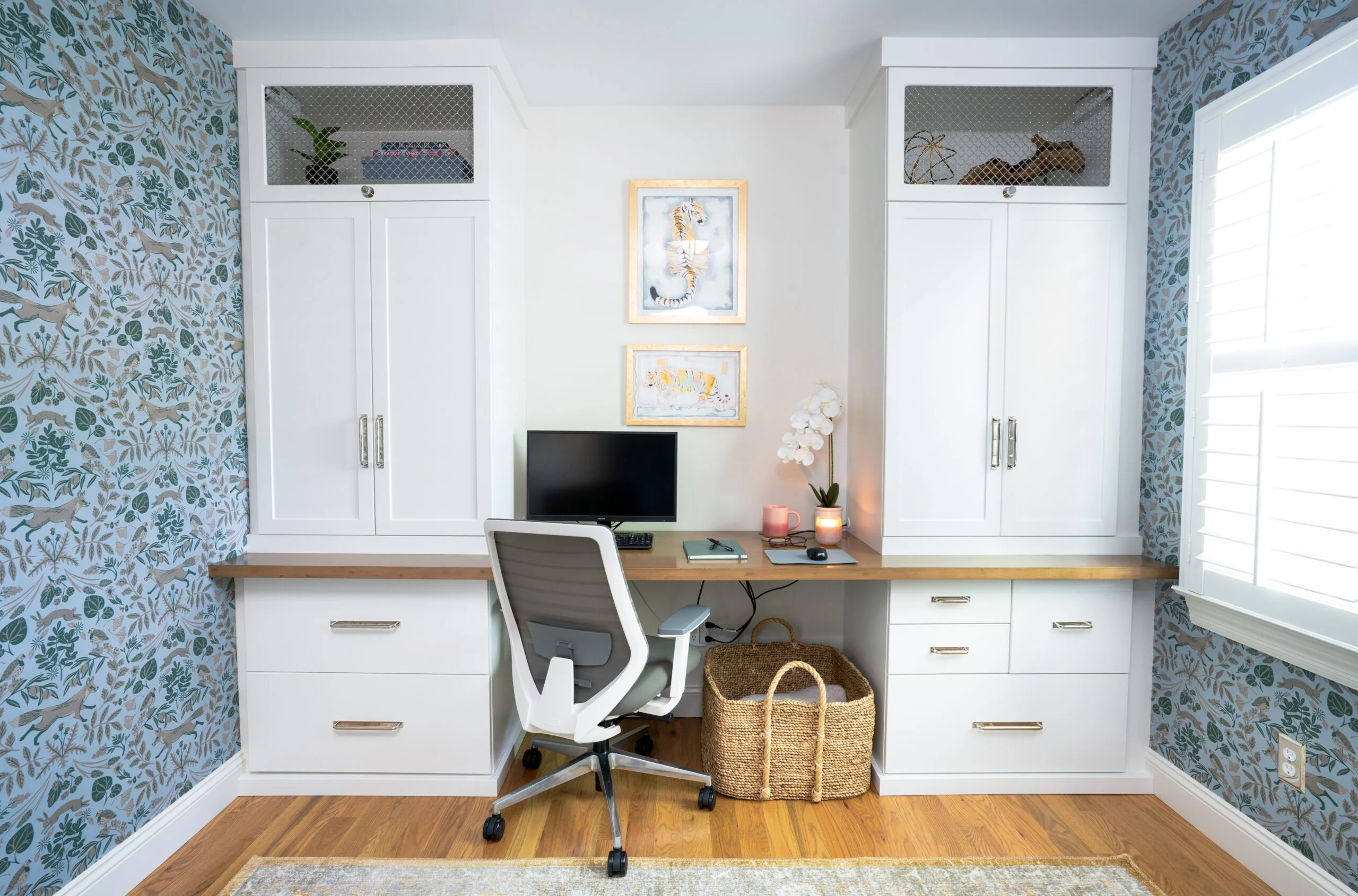 Built-in white desk with wooden countertop, gray chair, and patterned wallpaper.