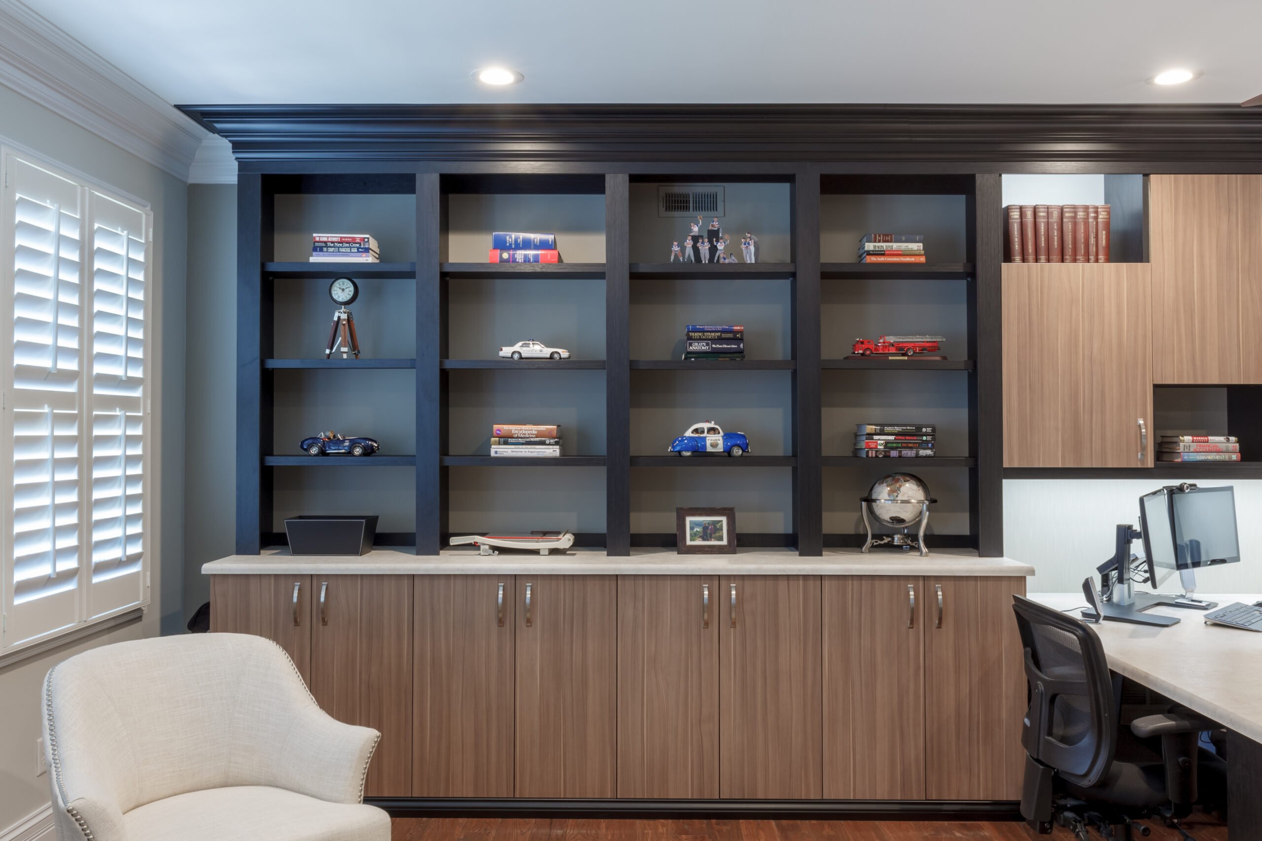 Custom home office with dark wood shelves and light wooden cabinets, featuring decorative objects, books, and a computer workstation.
