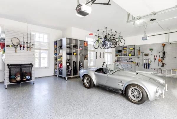 A bright and organized two-car garage with a silver gray Shelby Cobra parked on a gray speckled floor.