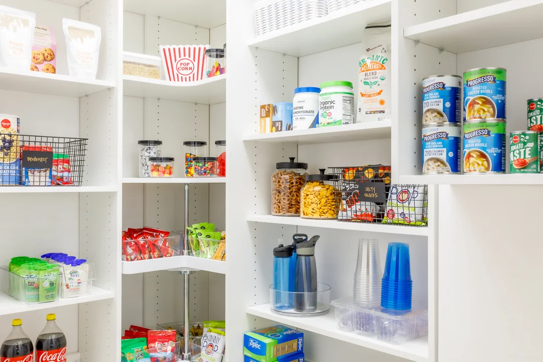 Organized white pantry shelving with snacks, drinks, canned goods, and household storage.