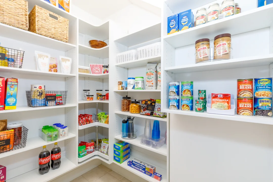White organized pantry, shelves filled with cereal, snacks, canned goods, peanut butter, and baking supplies.
